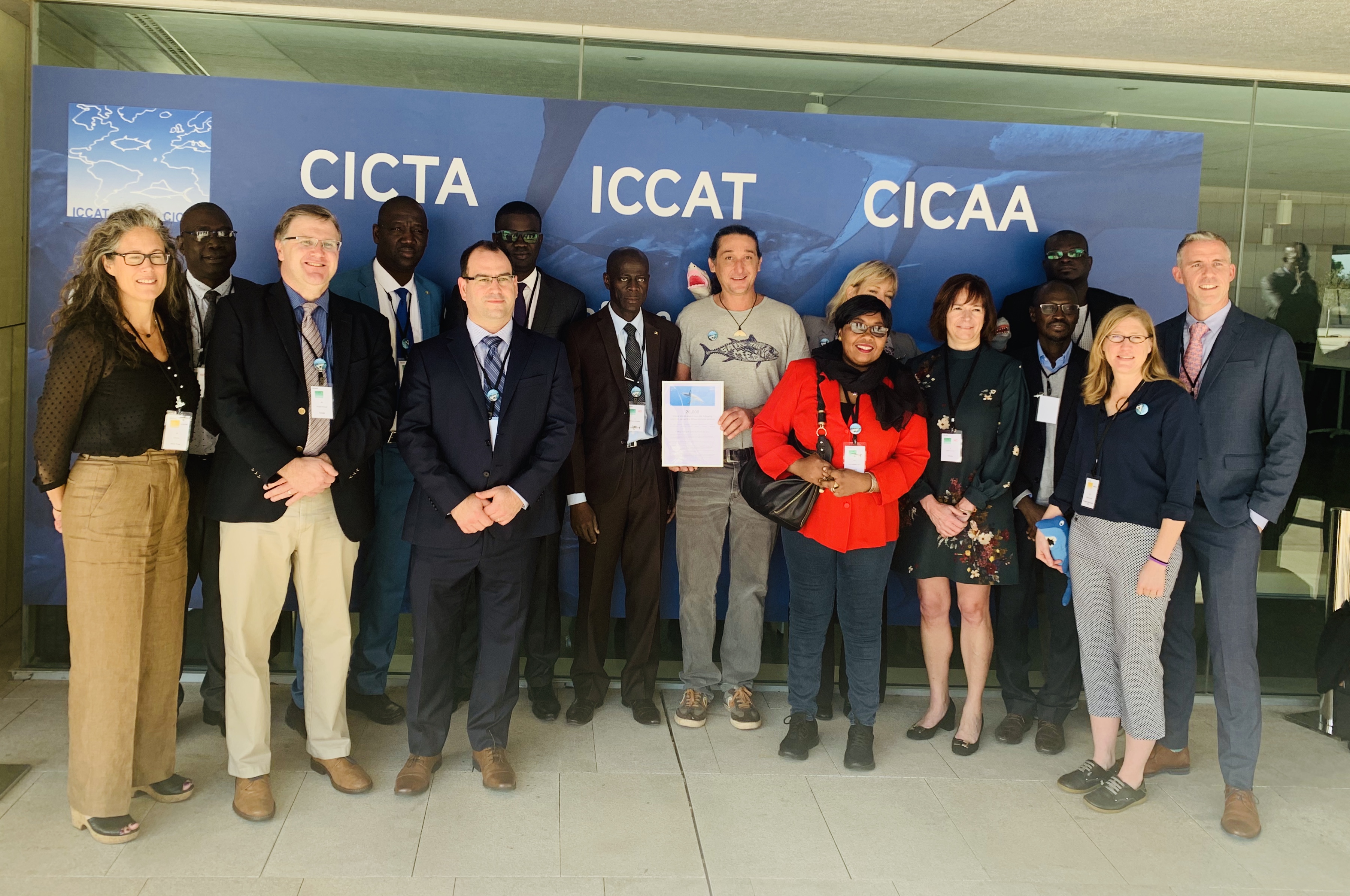 A group of fifteen people stand in front of an ICCAT banner