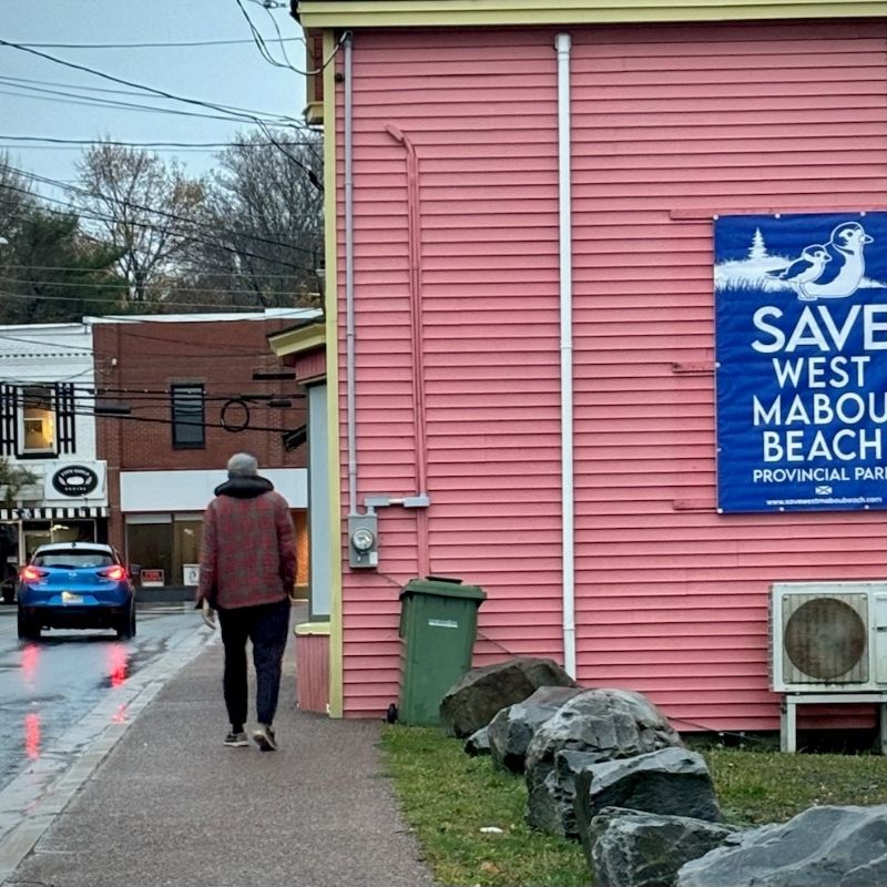 Pink side of a building with a large Save West Mabou Beach Provincial park sign
