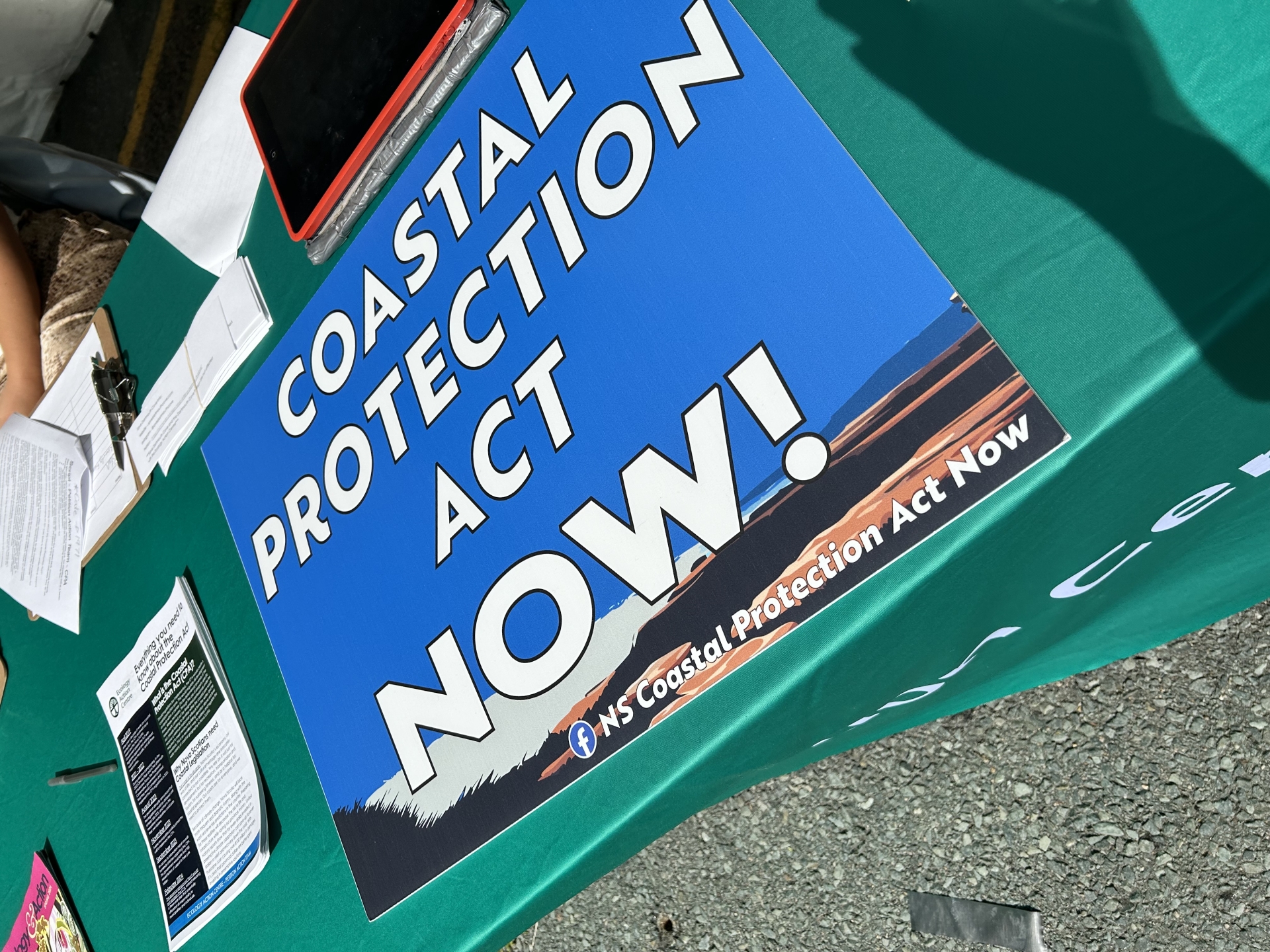 a sign that says "Coastal Protection Act NOW" on a green table