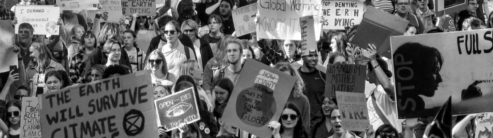 black and white image of a crowd of protestors filling the full width of a street, many holding signs about climate change