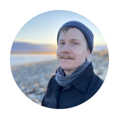 Circular headshot of Scott wearing a scarf and hat and smiling