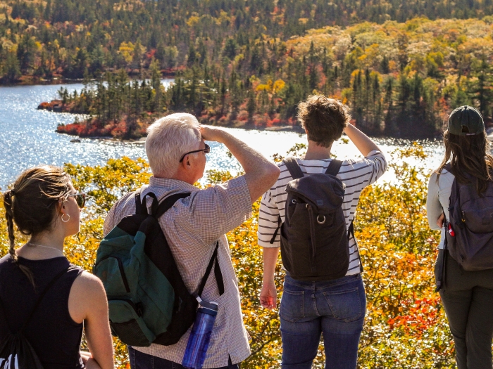 Four people looking out over a lake with fall colours, yellow tree leaves.