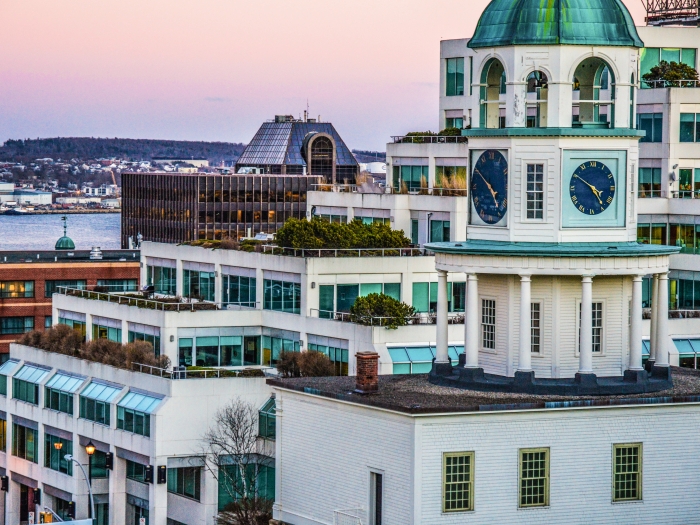 Halifax's white old town clock at sunset with building and the Halifax harbour in the background.