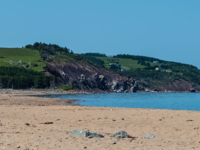 View of West Mabou Beach with rolling hillside, farm houses and blue sky in the background