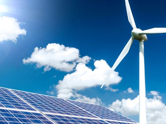 A blue sky with the sun peaking out from behind a cloud. Below a solar panel and windmill can be seen
